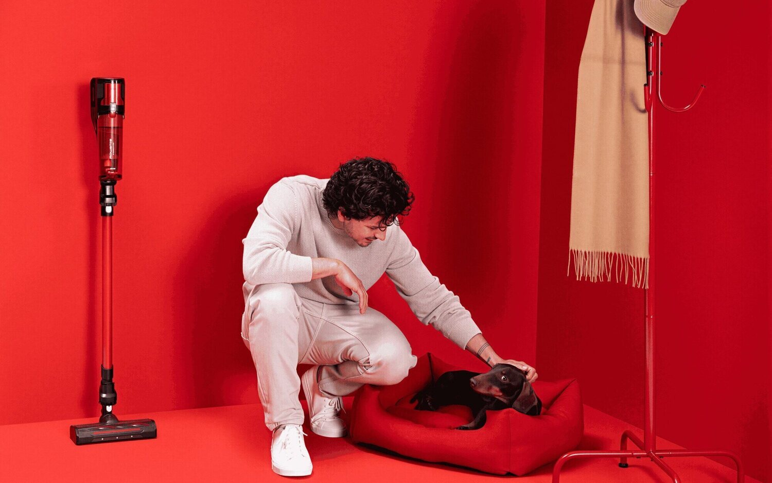 Hombre acariciando a un perro junto a una aspiradora sin cable